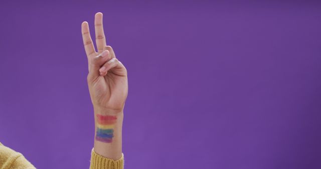 Hand showing a peace sign with a rainbow LGBTQ+ tattoo against a purple backdrop. Ideal for use in campaigns promoting LGBTQ+ rights, equality, and diversity. Useful for articles, blogs, posters, and social media posts celebrating love, freedom, and human rights.