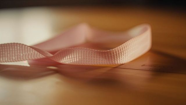 Soft pale pink woven ribbon resting on warm wooden surface with shallow focus and bokeh