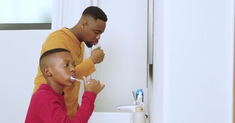 Father and son practicing dental hygiene in bathroom