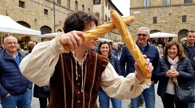 Street performer juggling baguettes in medieval italian square entertaining market crowd