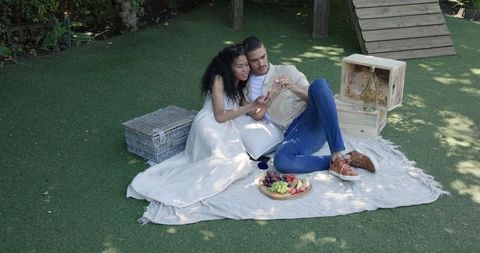 Couple Enjoying Picnic Outdoors with Smartphone in Garden