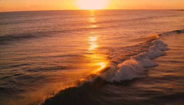 Golden sunset path across ocean with cresting wave and reflective horizon at dusk