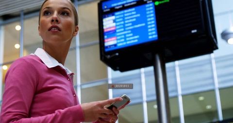 Young woman checking flight status on smartphone at modern airport terminal display