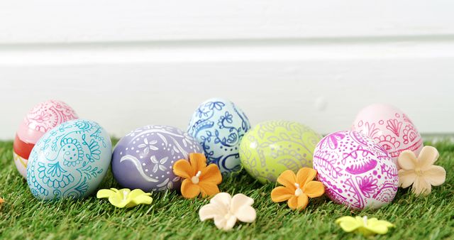 Colorful, intricately decorated Easter eggs arranged on green grass with scattered orange and yellow flowers. Ideal for use in Easter-themed designs, greeting cards, holiday promotions, and spring celebration advertisements.