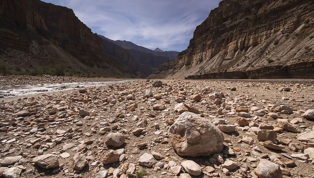 Giant boulder sitting on rocky canyon riverbed under layered sandstone cliffs