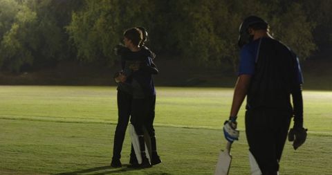 Teen cricket teammates hugging under floodlights on night field showing sportsmanship