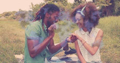 Placing engagement ring during sunlit picnic proposal, smiling couple in meadow