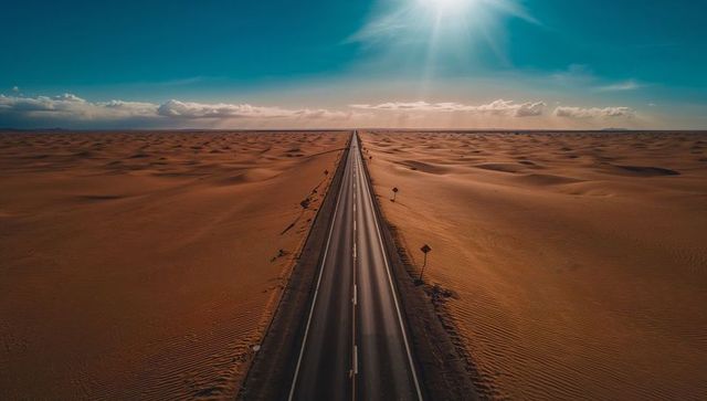 Stretching straight highway cutting through sunlit desert dunes toward distant horizon