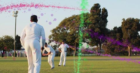 Cricket teammates fielding on park outfield during practice with colorful paint streaks