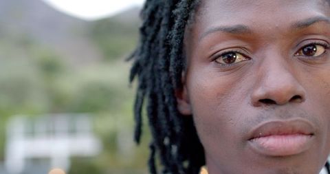 Close-up portrait African American man with dreadlocks gazing into camera outdoors calm