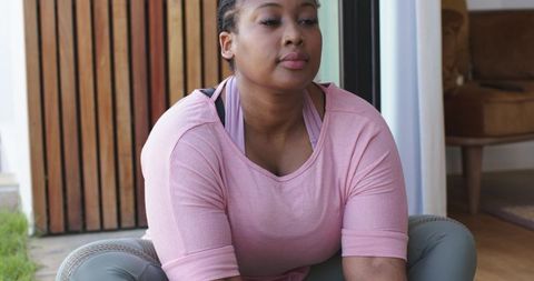African american woman practicing mindful stretching in home doorway wearing pink top and gray leggi