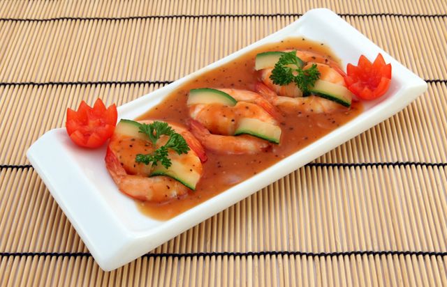 Elegant shrimp appetizer presented on white rectangular plate, topped with savory sauce, garnished with gourd slices and parsley, ideal for culinary menus, food blogs, restaurant promotions, and gourmet recipe presentations.
