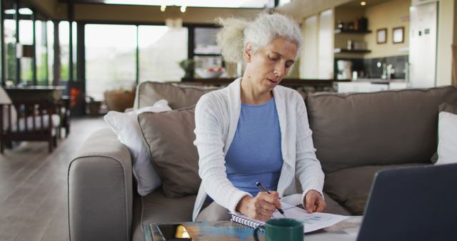 Senior biracial woman sitting on sofa taking notes. retirement and senior lifestyle, spending time alone at home.