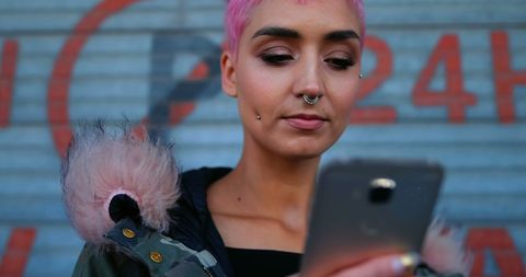 Trendy young woman texting against graffiti wall