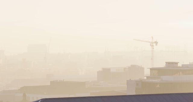 Urban skyline enveloped in fog at dawn with a construction crane and buildings visible across the horizon. This serene and misty scene is perfect for illustrating the stillness of early mornings in city centers, urban development, or construction-related themes.