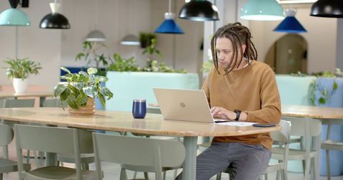 African American man working on laptop in modern coworking space with plants