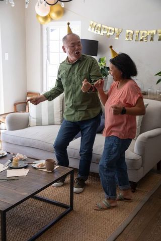 Senior asian couple dancing and singing at home birthday celebration
