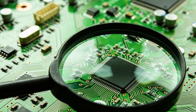 Magnifying glass revealing microchip and copper traces on green PCB circuit board close-up