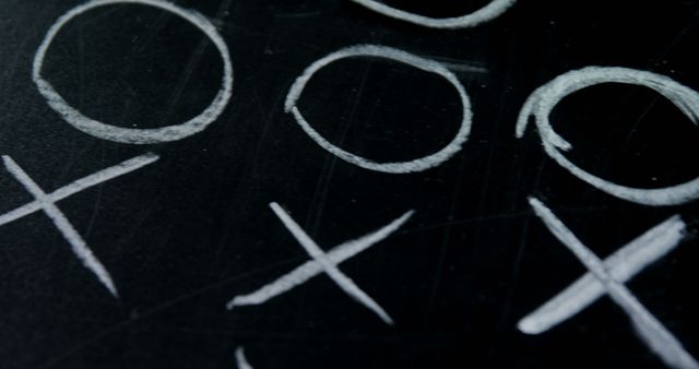Close-up view of a tic tac toe game drawn with chalk on a black chalkboard. Useful for educational materials, strategy game resources, and children's activity illustrations.