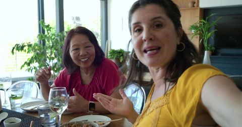 Diverse female friends dining at home, sharing meal and conversation over wine