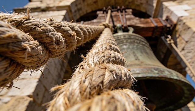 Climbing thick braided rope toward historic church bell with weathered patina and texture