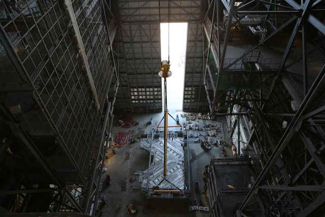 Depicts the precise engineering and technological advancements at NASA’s Kennedy Space Center. Shows a heavy-lift crane lifting the C-level work platforms in the Vehicle Assembly Building. Suitable for use in educational materials, articles on space exploration, or projects showcasing engineering and technology. Ideal for content related to NASA’s missions, space travel, and infrastructure preparations for future expeditions.