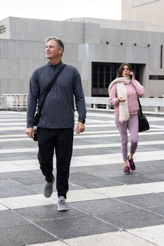 Active urban commuters walking tiled plaza in athleisure, smartphone call, shoulder bags