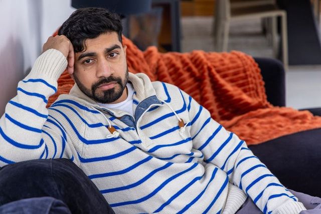 Man reclining on sofa wearing striped sweater with orange throw, cozy contemplative home portrait
