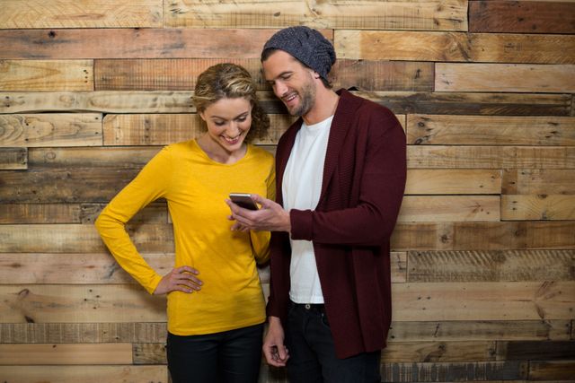 Couple using mobile phone in cafÃ© against wooden wall