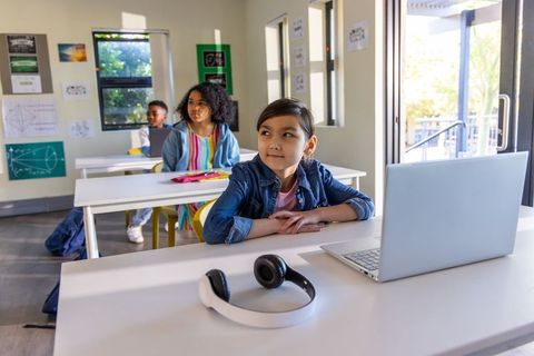 Multicultural children learning with laptop and headphones in sunlit modern classroom