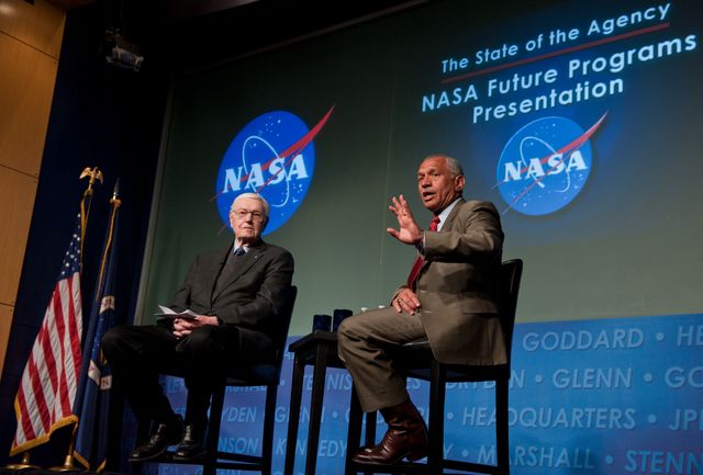 Former NASA Administrator James Beggs and present NASA Administrator Charles Bolden are seen engaging in a dialogue about the future of NASA's space exploration programs at an event on March 4, 2011. The backdrop features the NASA logo, and an American flag is visible. This event, held at NASA Headquarters in Washington, is part of 'The State of the Agency: NASA Future Programs Presentation,' sponsored by the NASA Alumni League. Ideal for articles or publications on space exploration, NASA history, or aerospace advancements.