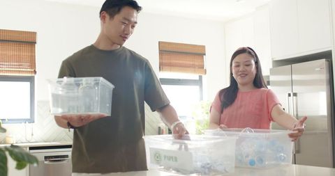 Asian couple sorting recyclables in sunlit modern kitchen promoting sustainable home living