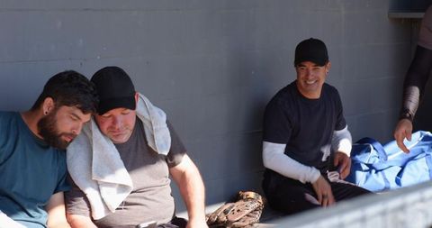 Baseball teammates sitting in dugout sharing relaxed moment with glove towel and duffel