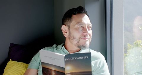 Mature Asian Man Relaxing with Book Baking in Sunlight