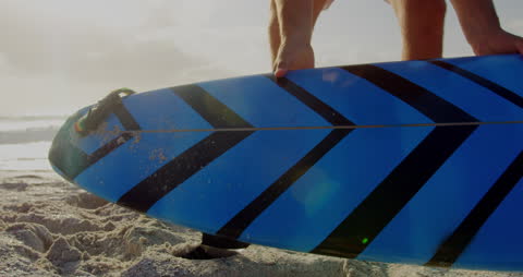 Surfer Picking Up Vibrant Blue Surfboard on Sunny Beach