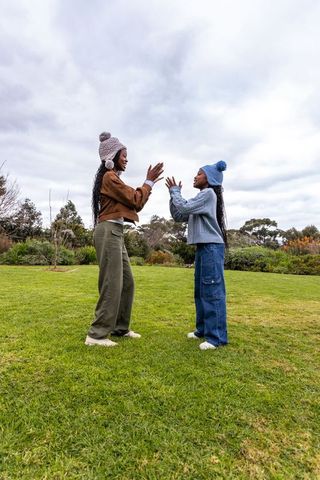 African american mother and teen daughter clapping together in park wearing pom-pom beanies