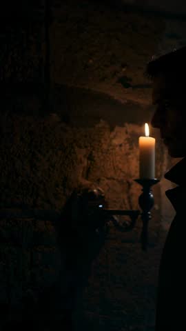 Entering man smothering sconce candle flame in dark stone corridor vertical suspense