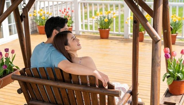 Couple relaxing on wooden porch swing surrounded by tulips on sunny spring deck romantic backyard