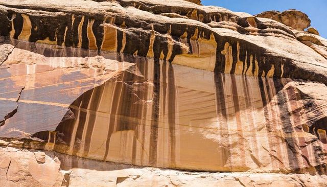 Sandstone cliff displaying dark varnish streaks, layered sedimentary bands, recessed alcove