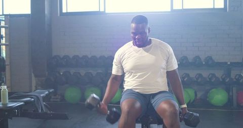 African American man performing seated dumbbell curls in bright gym for strength training