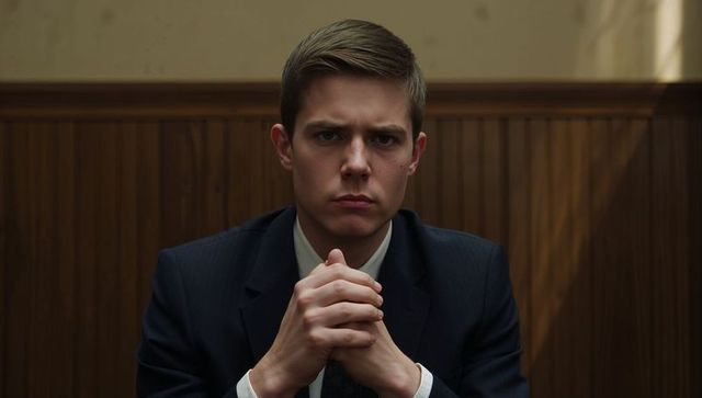 Intense young executive clasping hands in wood-panelled room looking determined low-light portrait