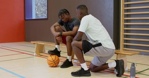 Basketball coach kneeling with african american player offering encouragement on bench