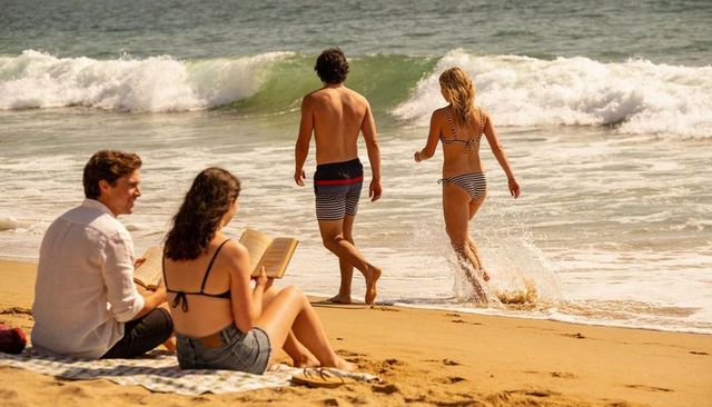 Sunlit beach afternoon with friends walking into surf and reading on towel