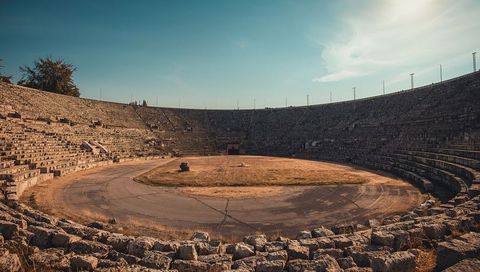 Sunlit ancient amphitheater featuring concentric stone tiers and central grass arena