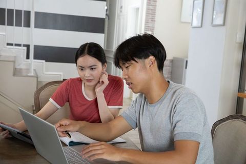 Two asian friends studying at home using laptop and tablet