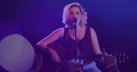 Solo female singer playing acoustic guitar under purple stage lights in intimate club