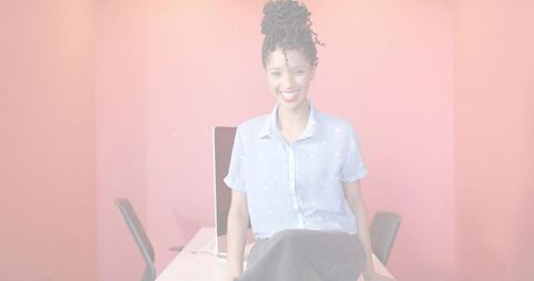 Smiling professional woman leaning on desk in minimalist pink office workspace