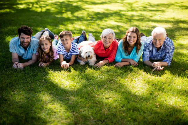 Multigenerational family lying on grass in park with dog, enjoying sunny day. Ideal for concepts of family bonding, outdoor activities, leisure time, and intergenerational relationships.
