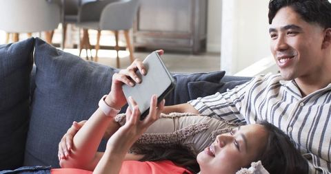 Young Couple Relaxing on Sofa Sharing Tablet and Smiling During Cozy Afternoon at Home