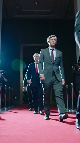 Corporate Delegation Walking Red Carpet Through Arch While Photographers Capturing Flashes